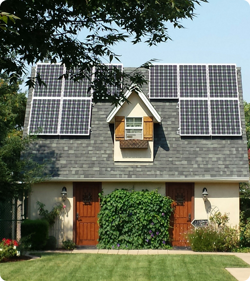 A small building with a gray shingled roof and solar panels installed on top, ideal for project management consulting. It features two wooden doors, a single dormer window with shutters, and green plants flourishing in front.