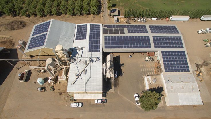 Aerial view of an industrial facility with large solar panels installed on the rooftops of multiple buildings in a rural area, possibly benefiting from a USDA REAP Grant.