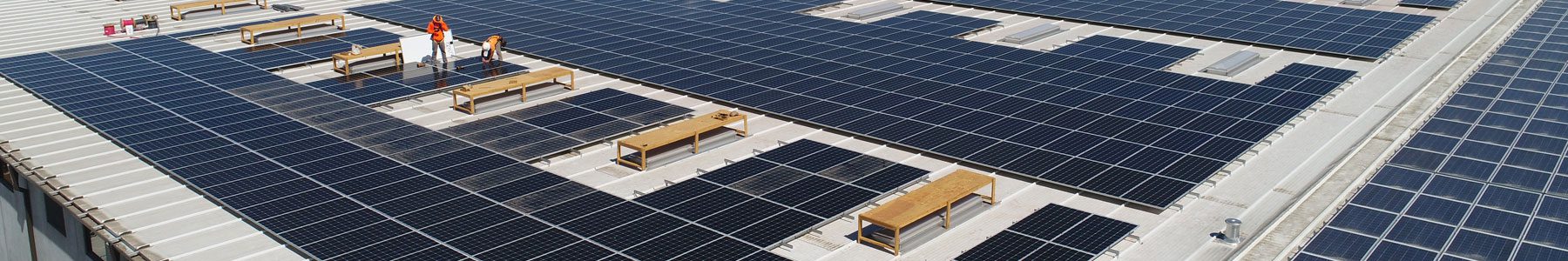 Aerial view of a large rooftop Solar PV Systems installation with several workers in the distance.